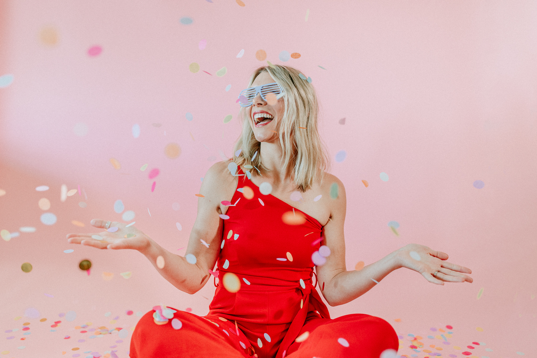 a physician's assistant and christian health coach celebrating with confetti in a red jumpsuit with a pink background